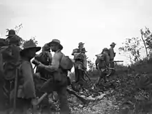 Soldiers wearing slouch hats and carrying rifles form up below a ridge line